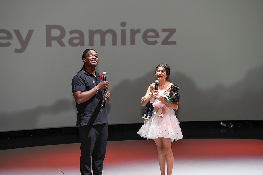 one person holding a microphone standing next to a person holding two dolls